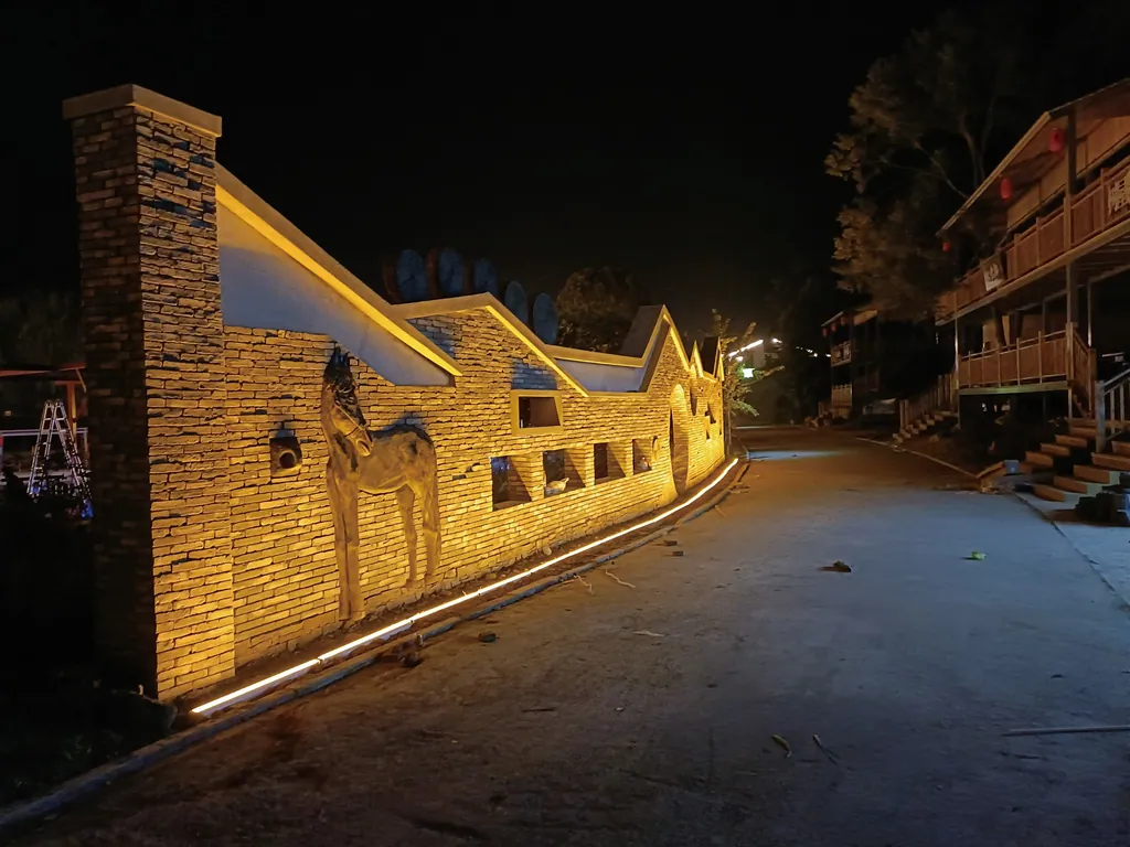 Illustrative application photo: Linear in-ground light grazing a stone wall with horse reliefs along a road at night.