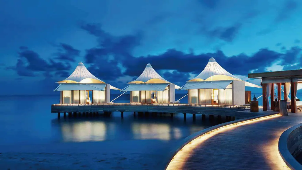 Illustrative application photo: Overwater villas and a curved boardwalk lit at dusk.