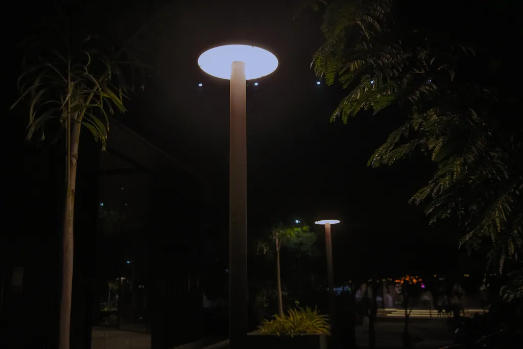 Disc post top lit at night beside palms, AWS-3 Commercial Tower