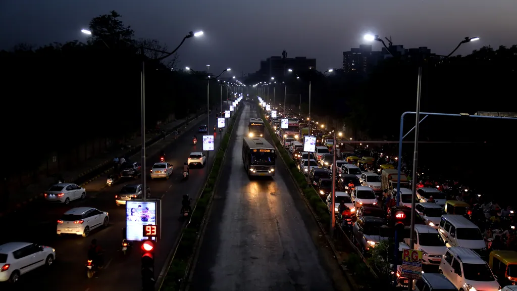 A bus in the dedicated BRTS lane at dusk, with traffic on both sides and street lights along the corridor