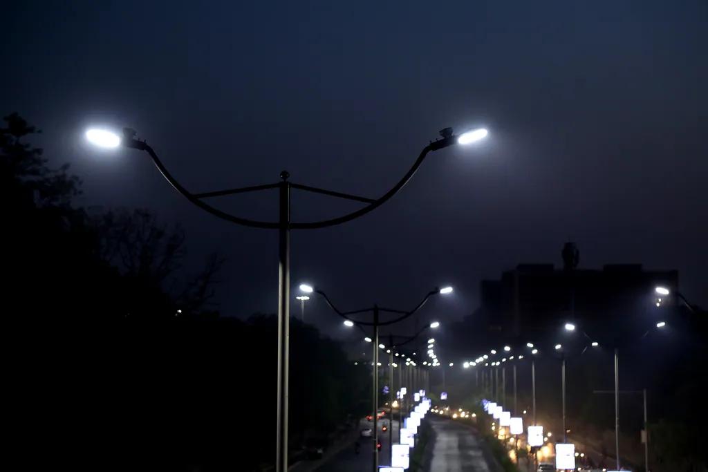 A double-arm street light pole in silhouette at dusk, with the lit corridor beyond