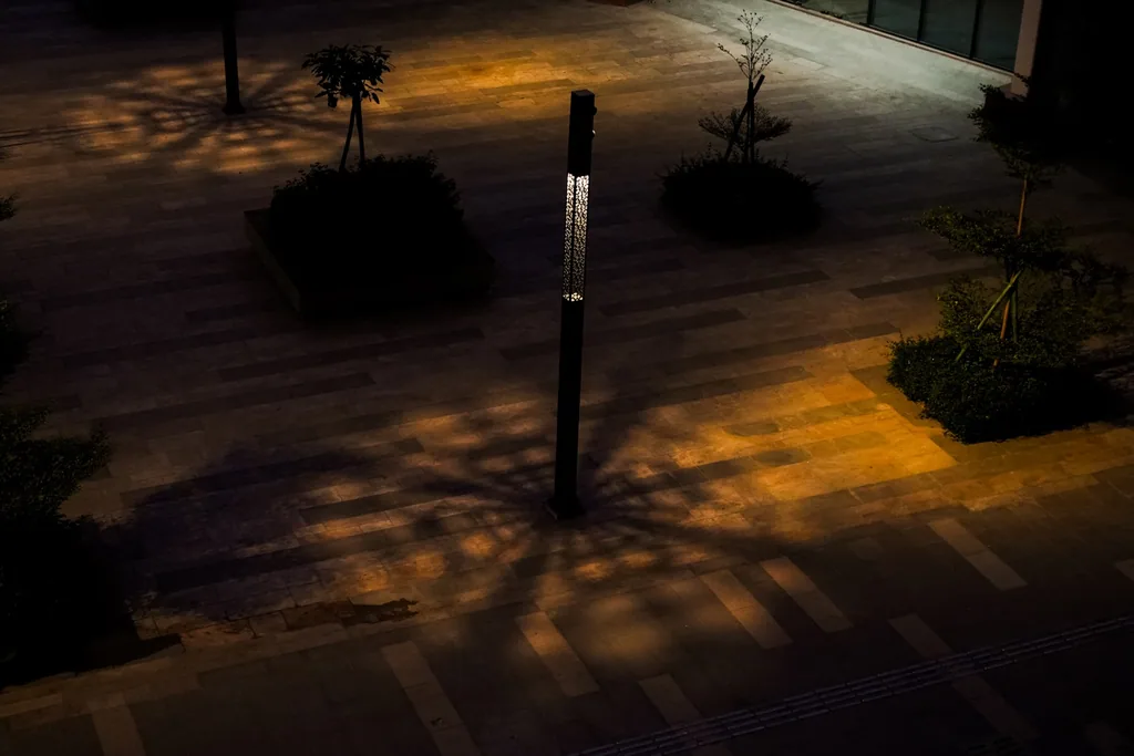 A Luméa pole with its laser-cut panel lit, casting a patterned pool of light on the paving