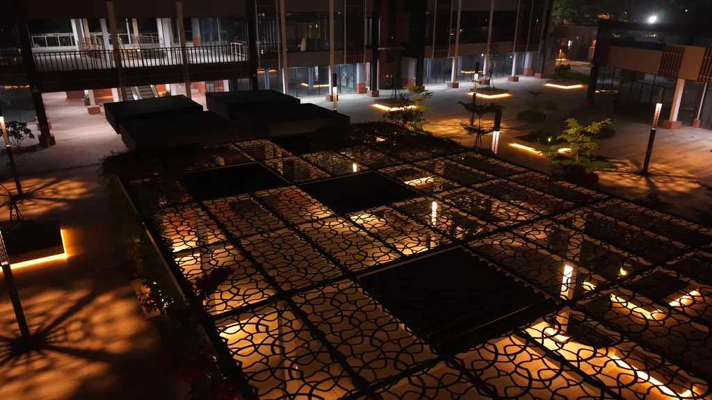 A pergola with a patterned metal canopy over the lit plaza at night