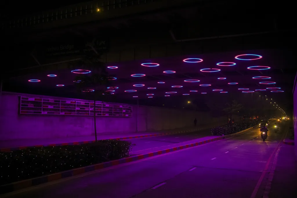 Motorcycles on the road beneath Nehru Bridge, with lit rings across the soffit
