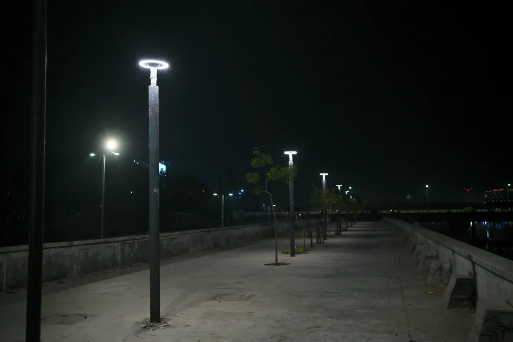 Ring post tops and young trees along a wide stretch of the riverfront promenade at night