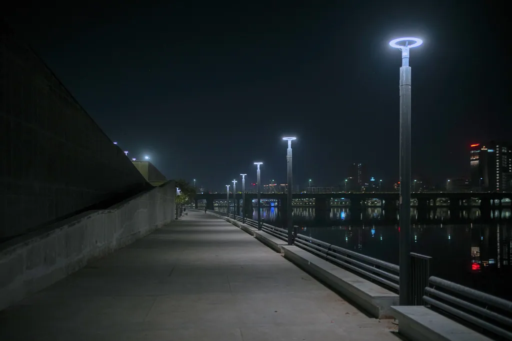 The promenade between a sloping wall and the river railing, lit by ring post tops