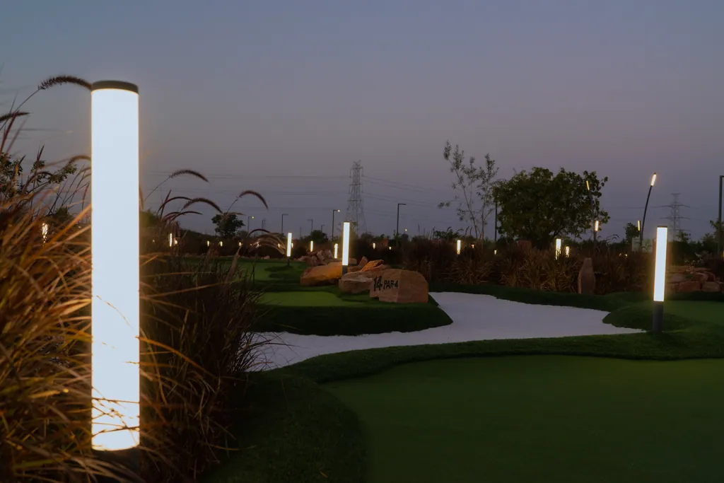 Lit tube bollard in the foreground of the putting course at dusk, with more bollards along the greens