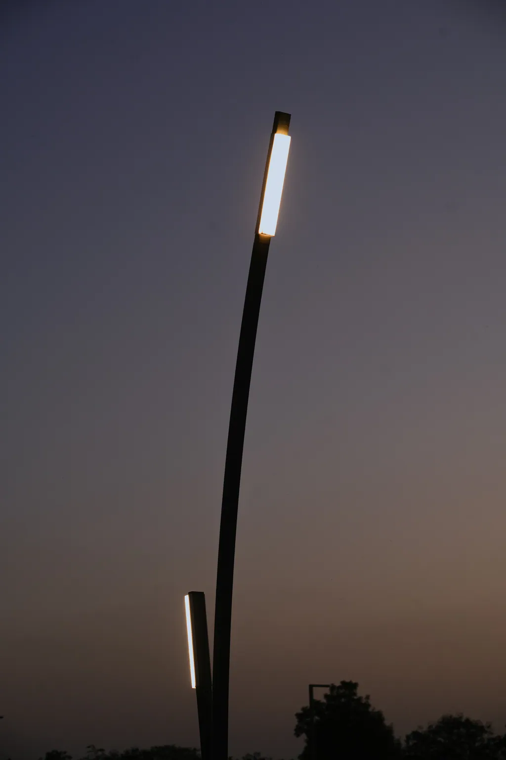 Curved pole with a lit linear head and a low linear post beside it at dusk