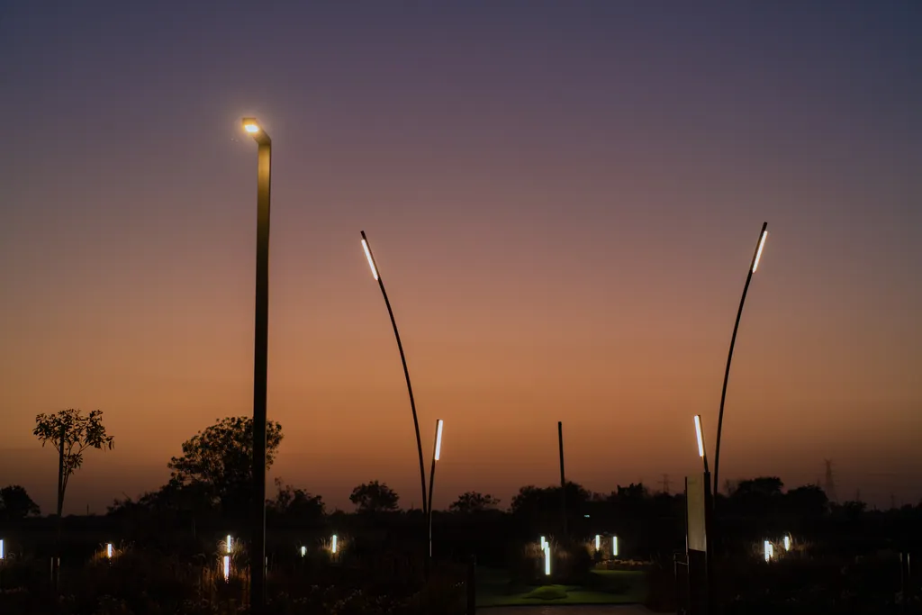 Single-arm pole and two curved poles with linear heads against a sunset sky, with bollards lit below