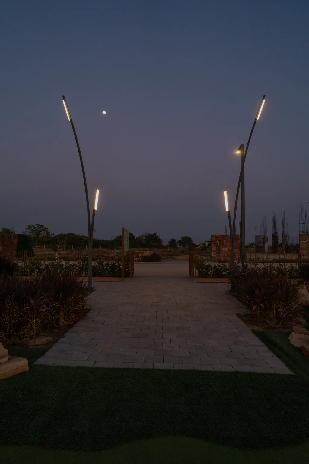 Paved path framed by two curved poles with lit linear heads at dusk