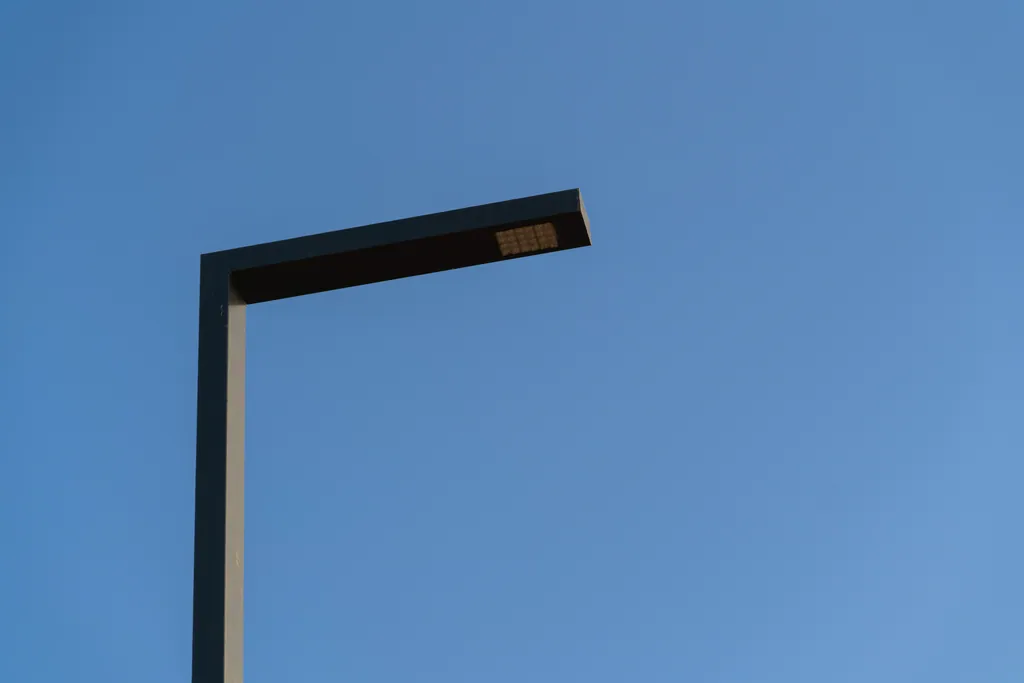 Head of a single-arm pole against a blue sky, showing the LED module in the underside of the arm