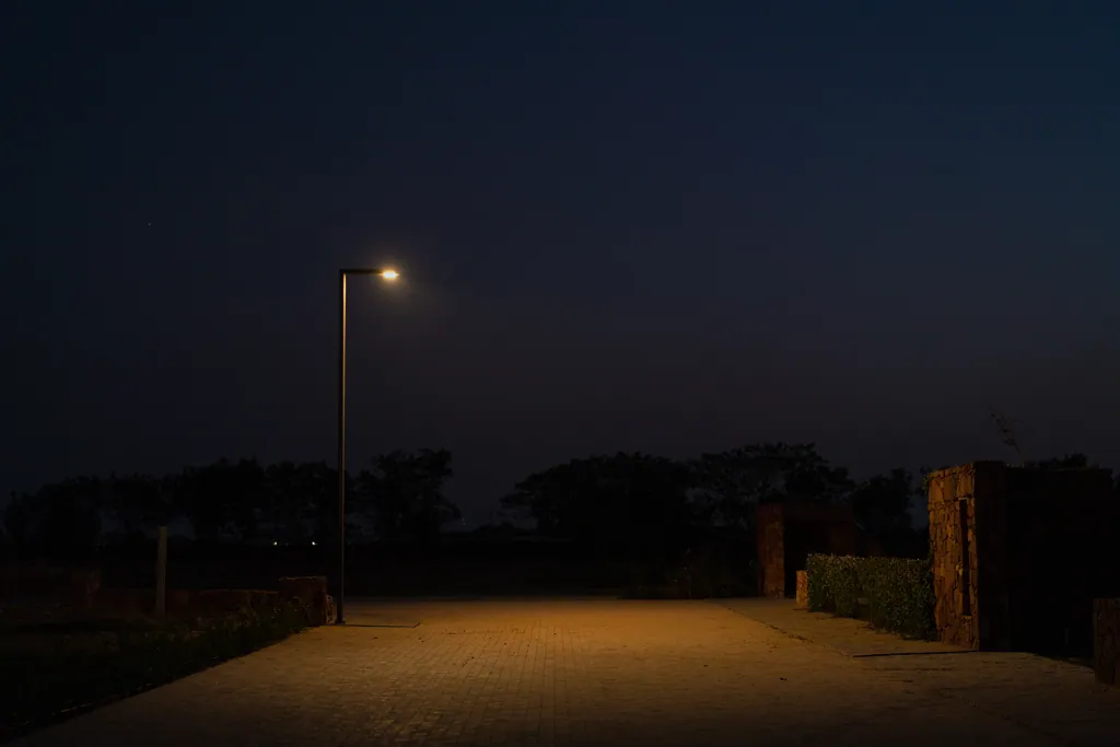 Single-arm pole casting warm light onto the promenade paving beside stone walls at night