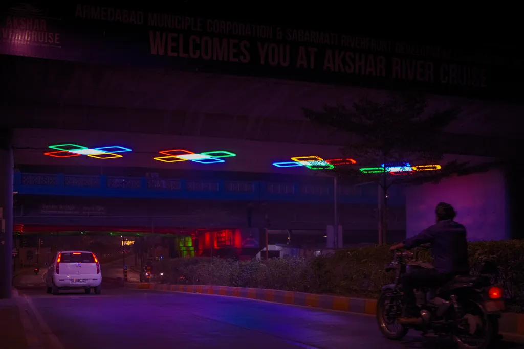 A car and a motorcyclist passing beneath the lit clusters of the VIP Underbridge